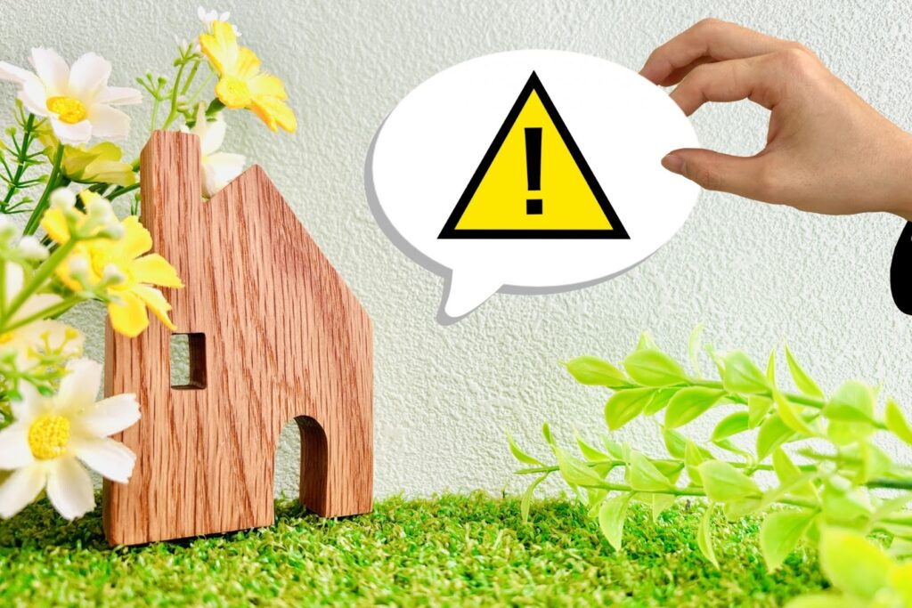 家の模型と注意マークを持った手