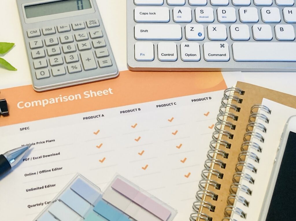 電卓やPCやノート、チェックリストが机に並んでいる画像